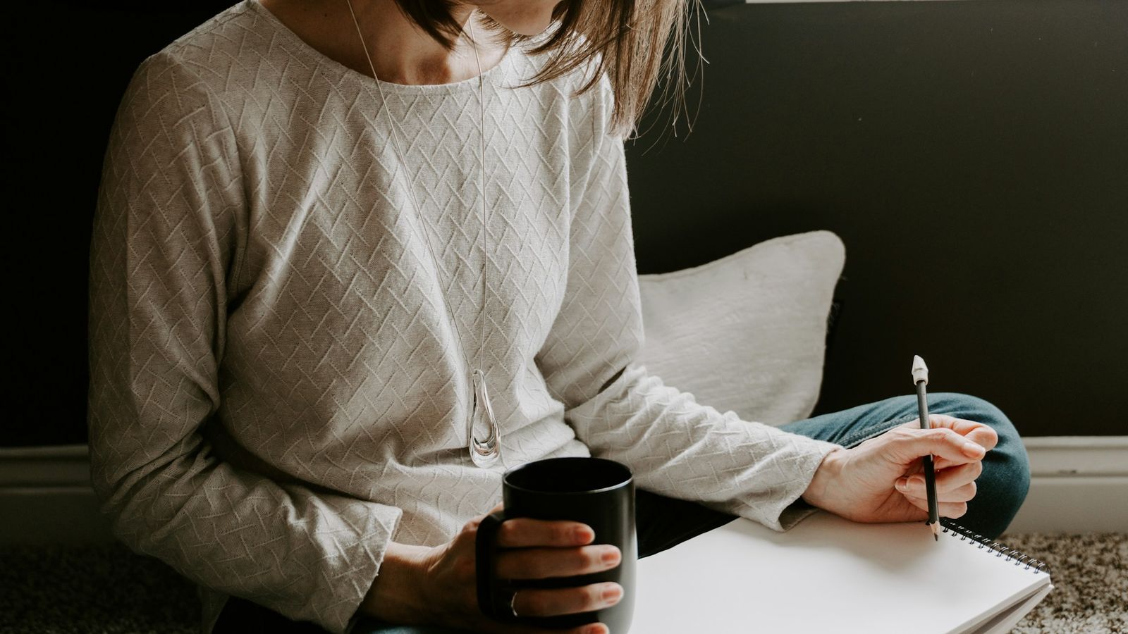 A woman holding a mug while writing notes in a notebook
