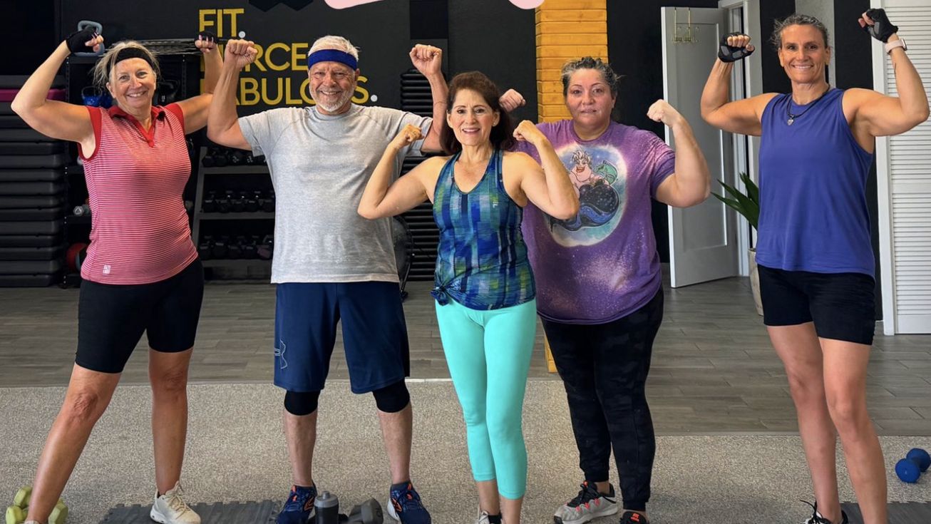 A smiling group flexing their arms together after a High In10sity Fitness class